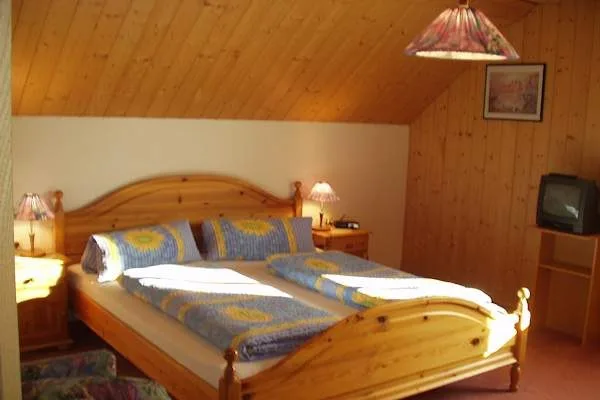 Gästezimmer mit heller Holzdecke, Doppelbett aus Massivholz, Nachtkästchen und Fernseher