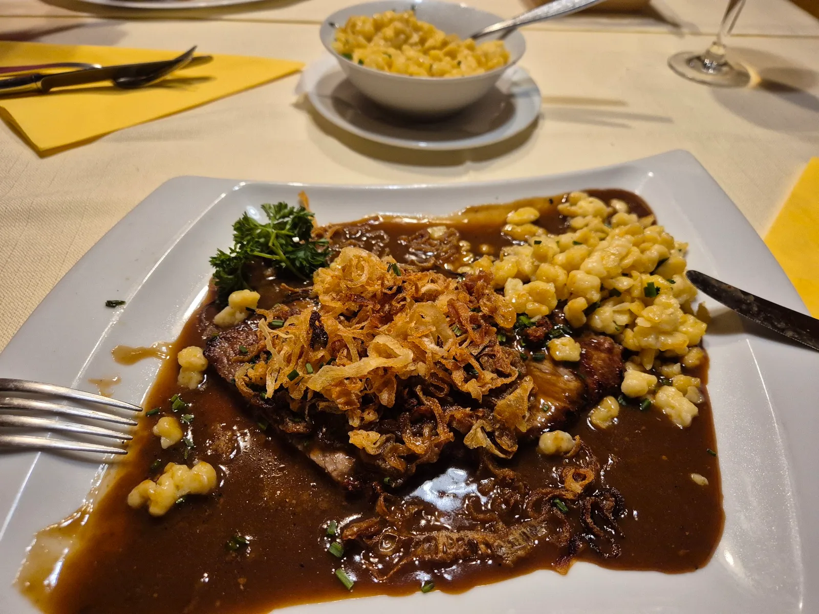 Zwiebelrostbraten mit knusprigen Röstzwiebeln, Butterspätzle und einer Schüssel Spätzle daneben